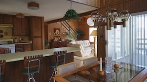 A spacious kitchen with wooden cabinets, a dining area with a glass table, and a living room with a sofa and a staircase. - 1970s Architecture & Design Cabin - The Lone Pine (Frazier Park)