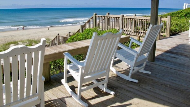 A wooden deck with white rocking chairs overlooking a beach. - Catalina Spectacular Oceanfront  4BR 4BA Duplex Addition & Major Renovation 2025 (Emerald Isle)