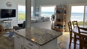 A modern kitchen with a large island, a dining area with a view of the ocean, and a cozy seating area with a view of the beach. - Catalina Spectacular Oceanfront  4BR 4BA Duplex Addition & Major Renovation 2025 (Emerald Isle)