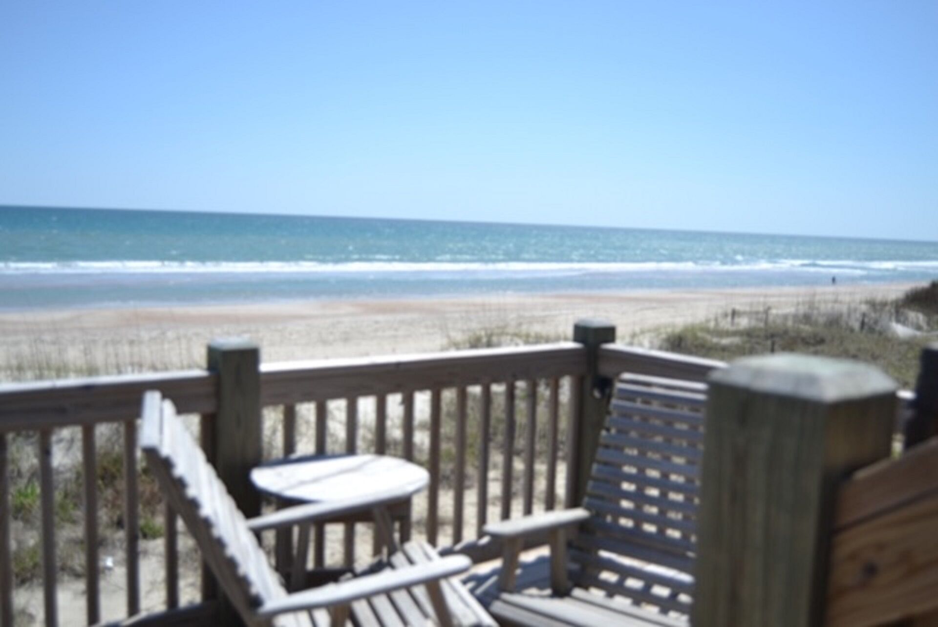 A wooden deck with a table and chairs overlooking a beach.