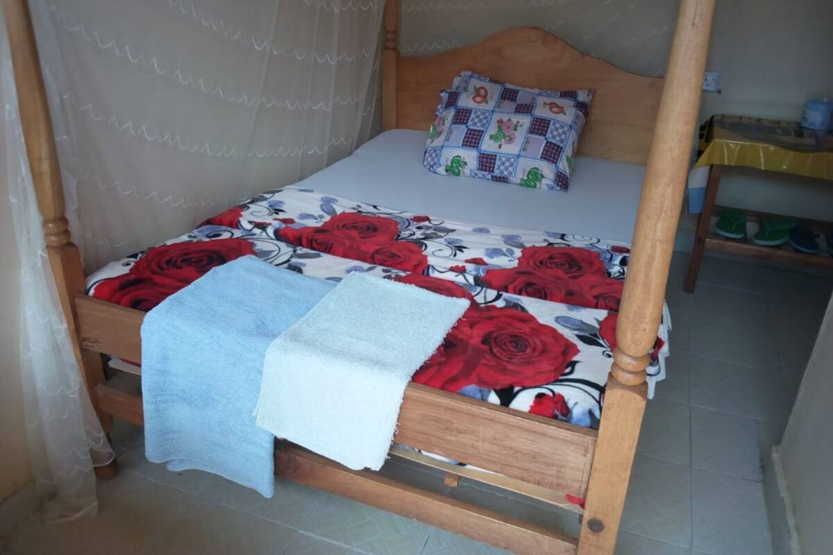Uma cama de solteiro com estrutura de madeira, colcha floral, travesseiro branco e manta azul.