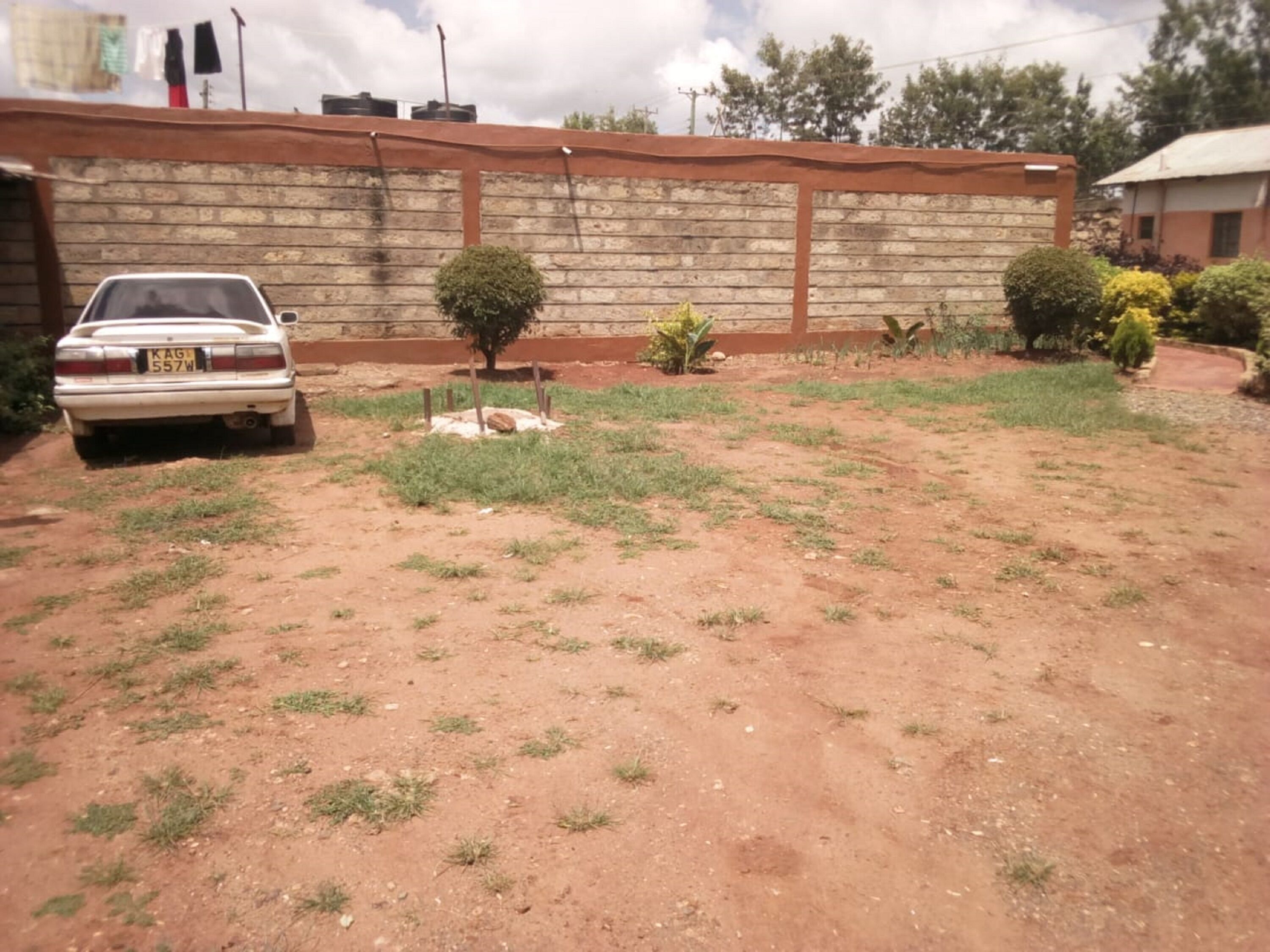 A dirt yard with sparse grass, a parked car, and a brick wall with a metal roof.