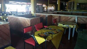 A restaurant with wooden booths and red chairs, featuring a yellow tablecloth with a sports team logo. - Mumbi Rose Guest House (Thika)