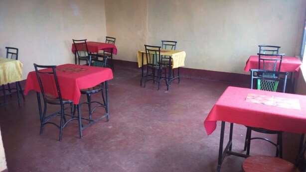 A room with several tables and chairs, some covered with red and yellow tablecloths. - Mumbi Rose Guest House (Thika)