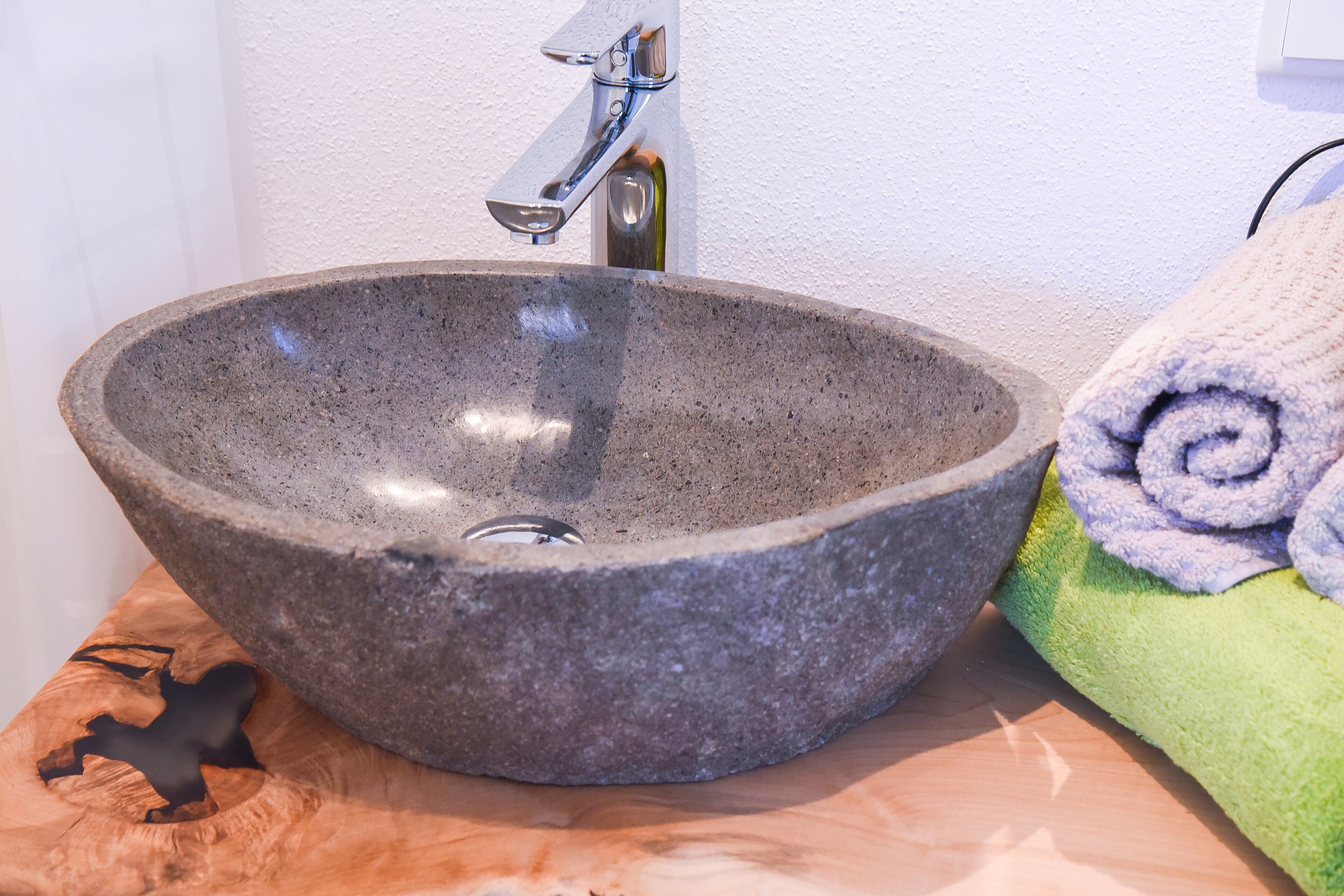 A stone sink with a modern faucet, a towel, and a wooden surface.