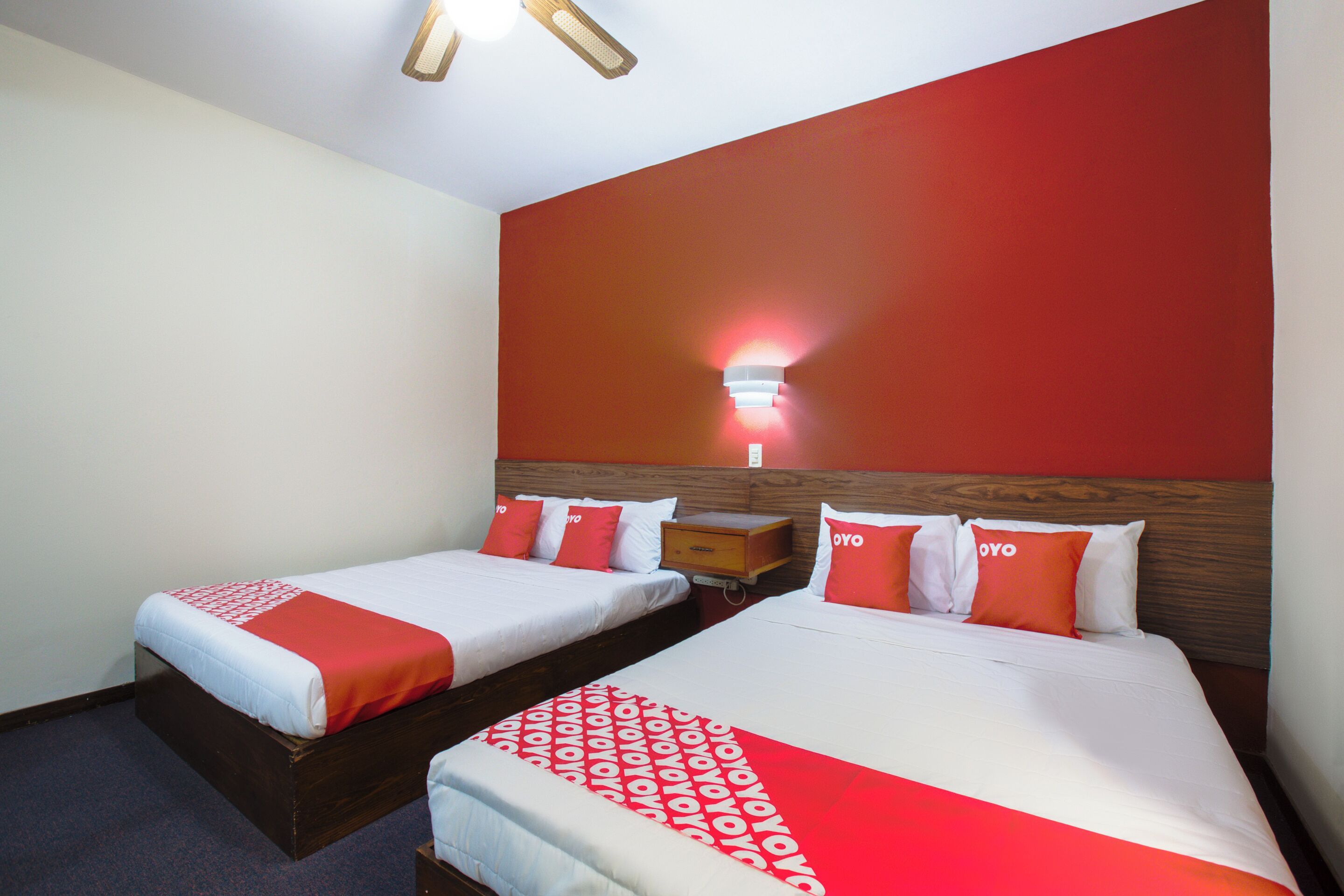Habitación de hotel con dos camas, cada una con ropa de cama roja y blanca, un cabecero de madera y una mesita de noche.