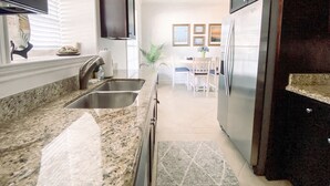 A kitchen with granite countertops, stainless steel appliances, and a dining area with a table and chairs. - Spectacular sunrise and ocean views! Award winning "Best Condo Rentals!" (Galveston)