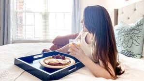 A person sitting on a bed with a tray of food and a drink. - Spectacular sunrise and ocean views! Award winning "Best Condo Rentals!" (Galveston)
