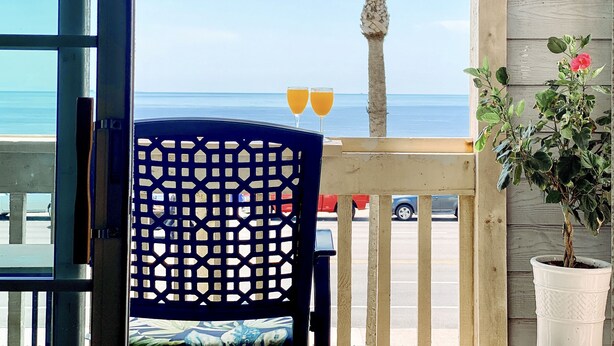A view from a balcony with a palm tree and a potted plant, overlooking a beach and a parking lot. - Spectacular sunrise and ocean views! Award winning "Best Condo Rentals!" (Galveston)