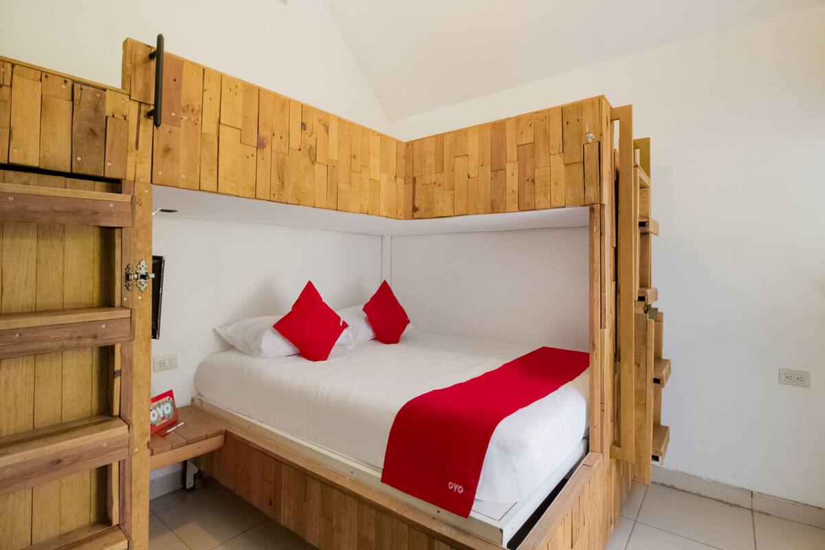 Una cama individual con estructura de madera, ropa de cama blanca y almohadas rojas.
