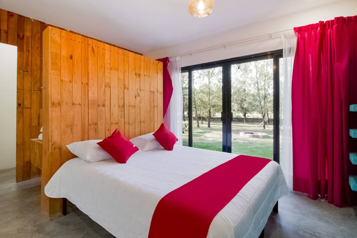 Un dormitorio con una cama grande, un panel de pared de madera y vistas a un jardín a través de un ventanal.
