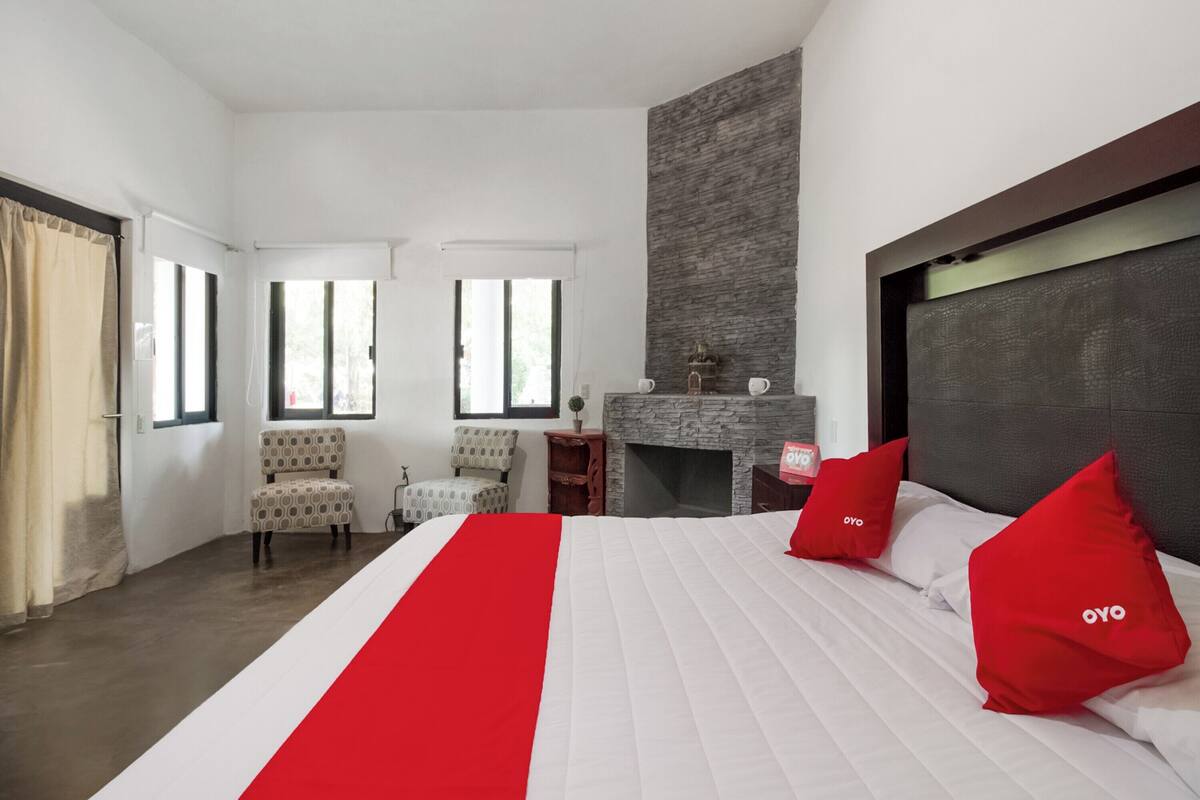Una habitación de hotel con una cama grande, una chimenea, dos sillones y vistas al exterior.