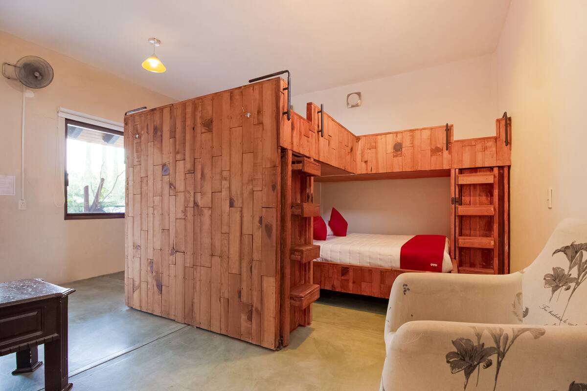 Una habitación con literas, un armario de madera, una mesita y una silla.