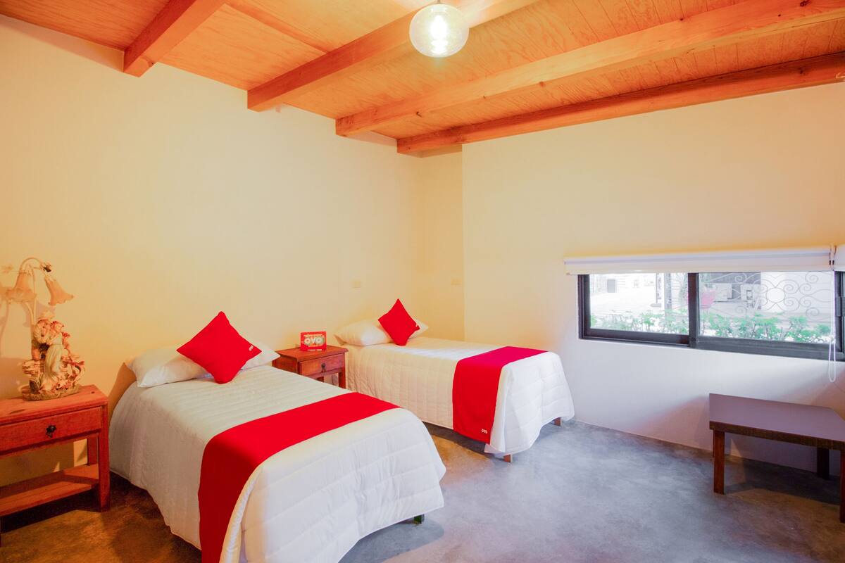Una habitación con dos camas, techo de madera, una ventana y un banco.