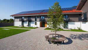 En moderne bygning med solpaneler på taget, en belagt gårdsplads og en cirkelformet bænk i midten.