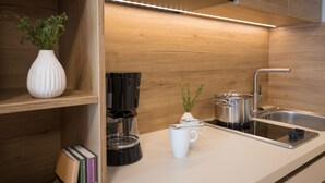 Et moderne køkken med træskabe, kaffemaskine, elkedel og en hvid kop på bordet.