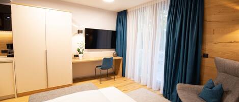 A modern hotel room with a bed, a desk with a chair, a TV, and a large window with curtains.