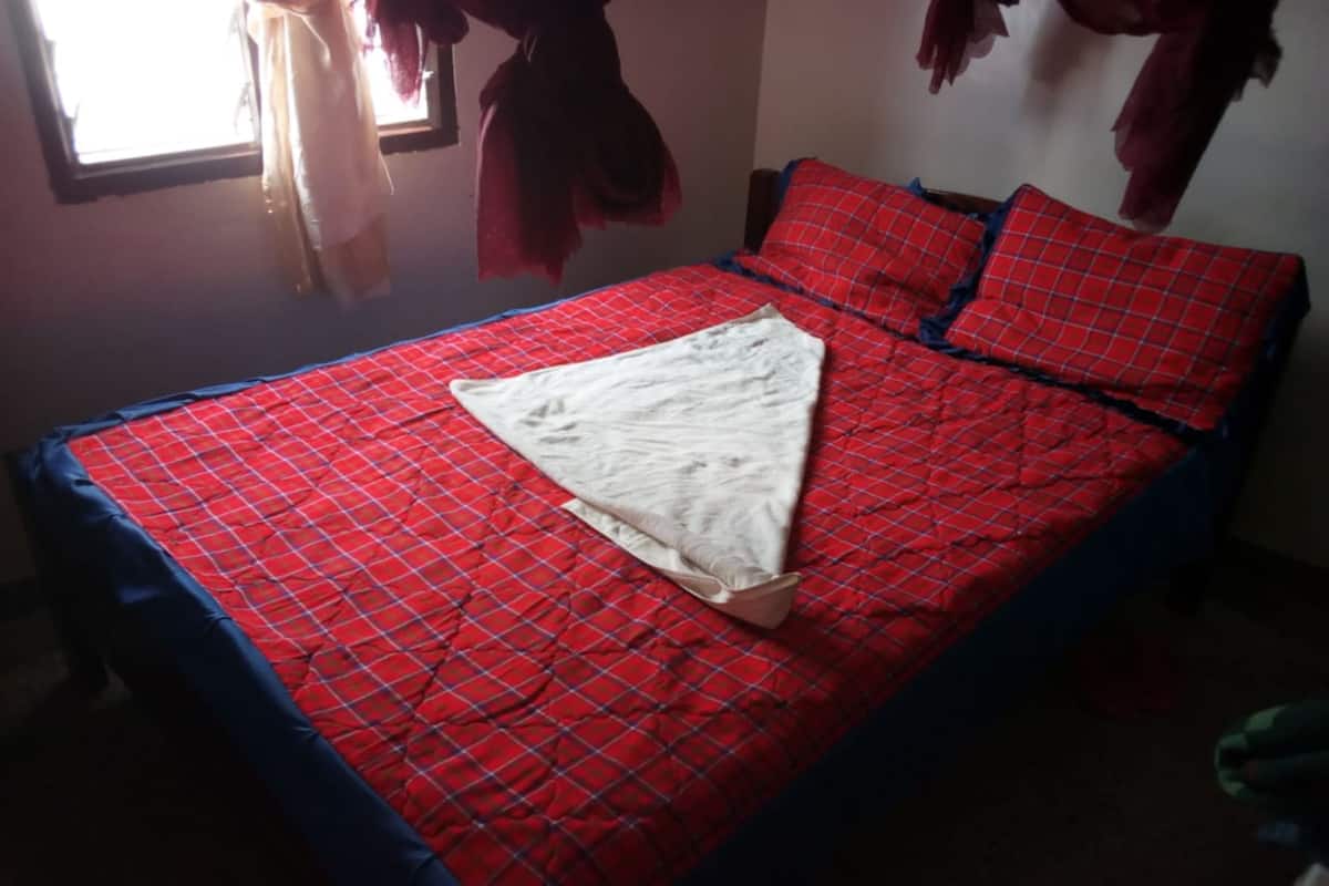 A bed with a red and blue checkered bedspread, a white pillow, and a red and blue pillow.