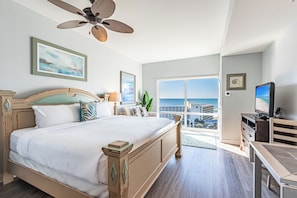 Quarto com uma cama grande, ventilador de teto, TV e vista para o mar.