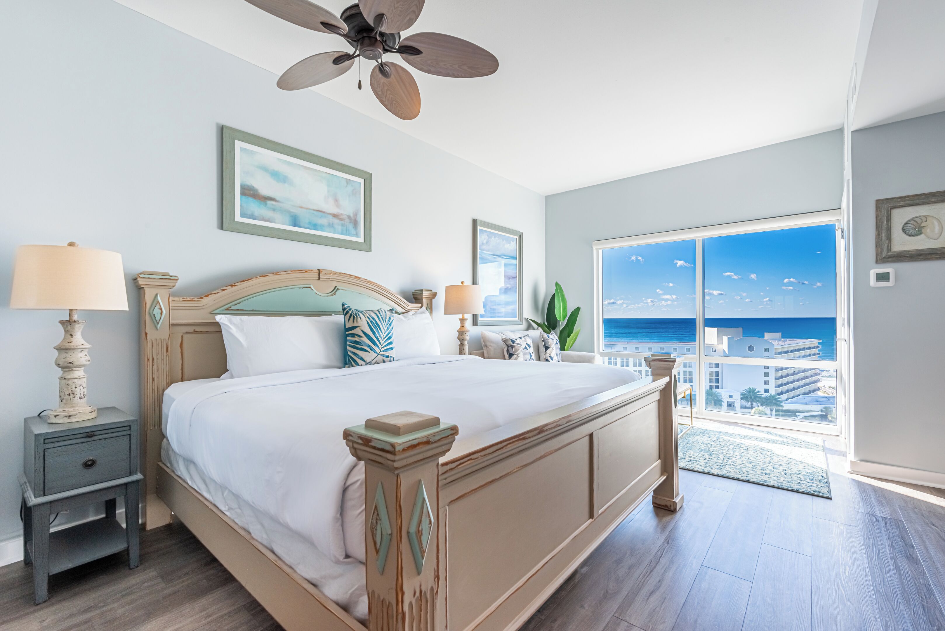 A bedroom with a large bed, a ceiling fan, and a view of the ocean through a large window.