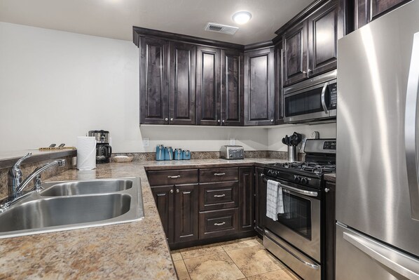 A kitchen with dark wood cabinets, stainless steel appliances, a double sink, and a granite countertop. - Close to Town, Ntl Parks & Trails | Pool & Hot Tub (Moab)