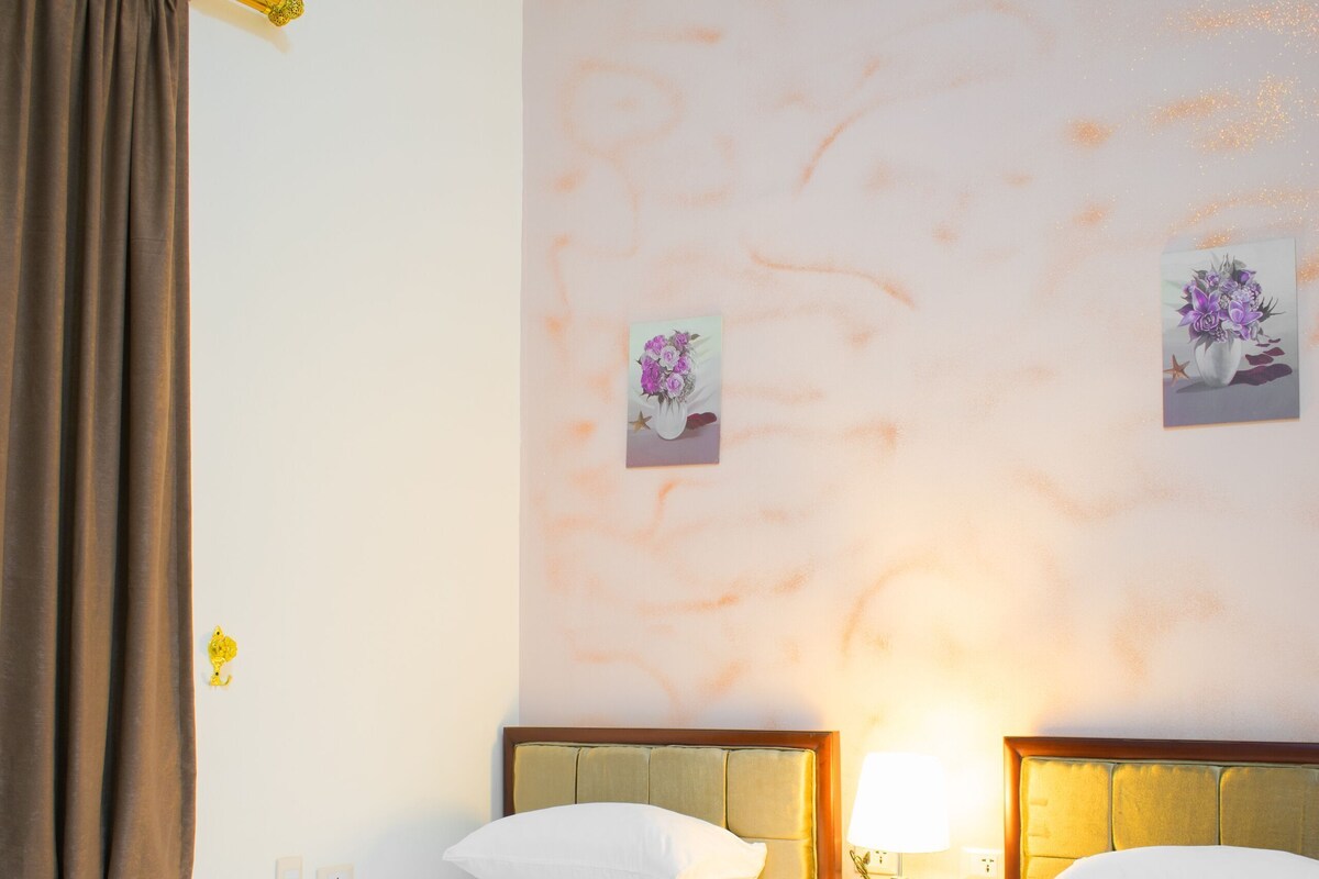 Ein Hotelzimmer mit zwei Betten, einer Klimaanlage, einer Wand mit floralem Wandbild und einem Vorhangfenster.