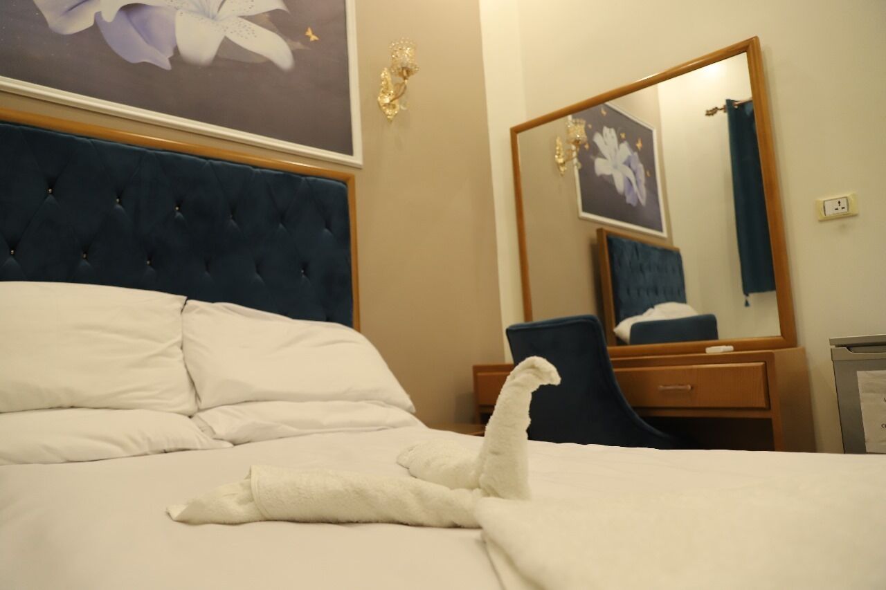 Una habitación de hotel con una cama grande, un aparador, un espejo y una pared con un cuadro floral.