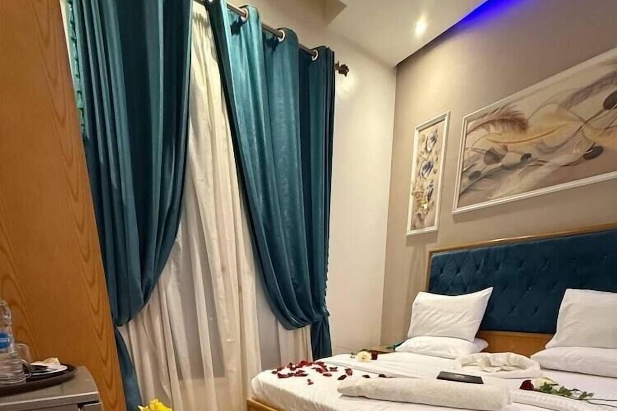 A bedroom with a bed, curtains, a painting, and a decorative arrangement of flowers and ribbons on the floor.