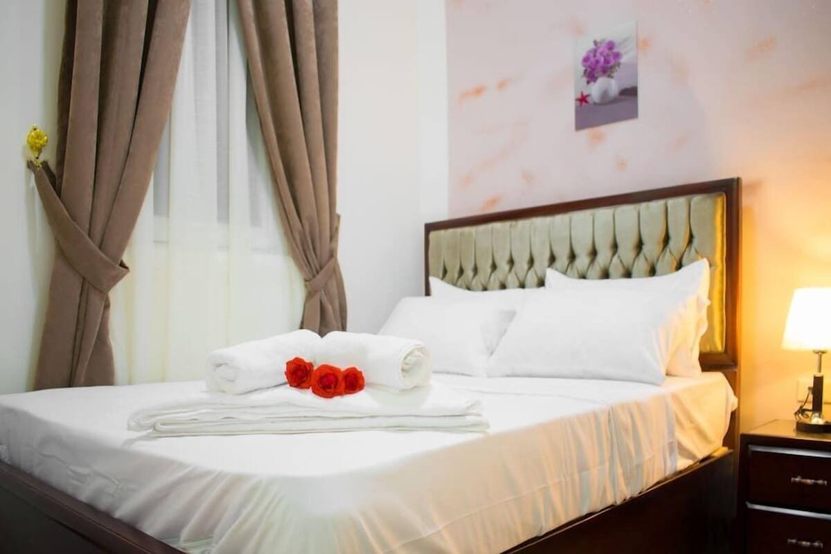 A neatly made bed with white linens, a headboard, and a bedside table with a lamp.