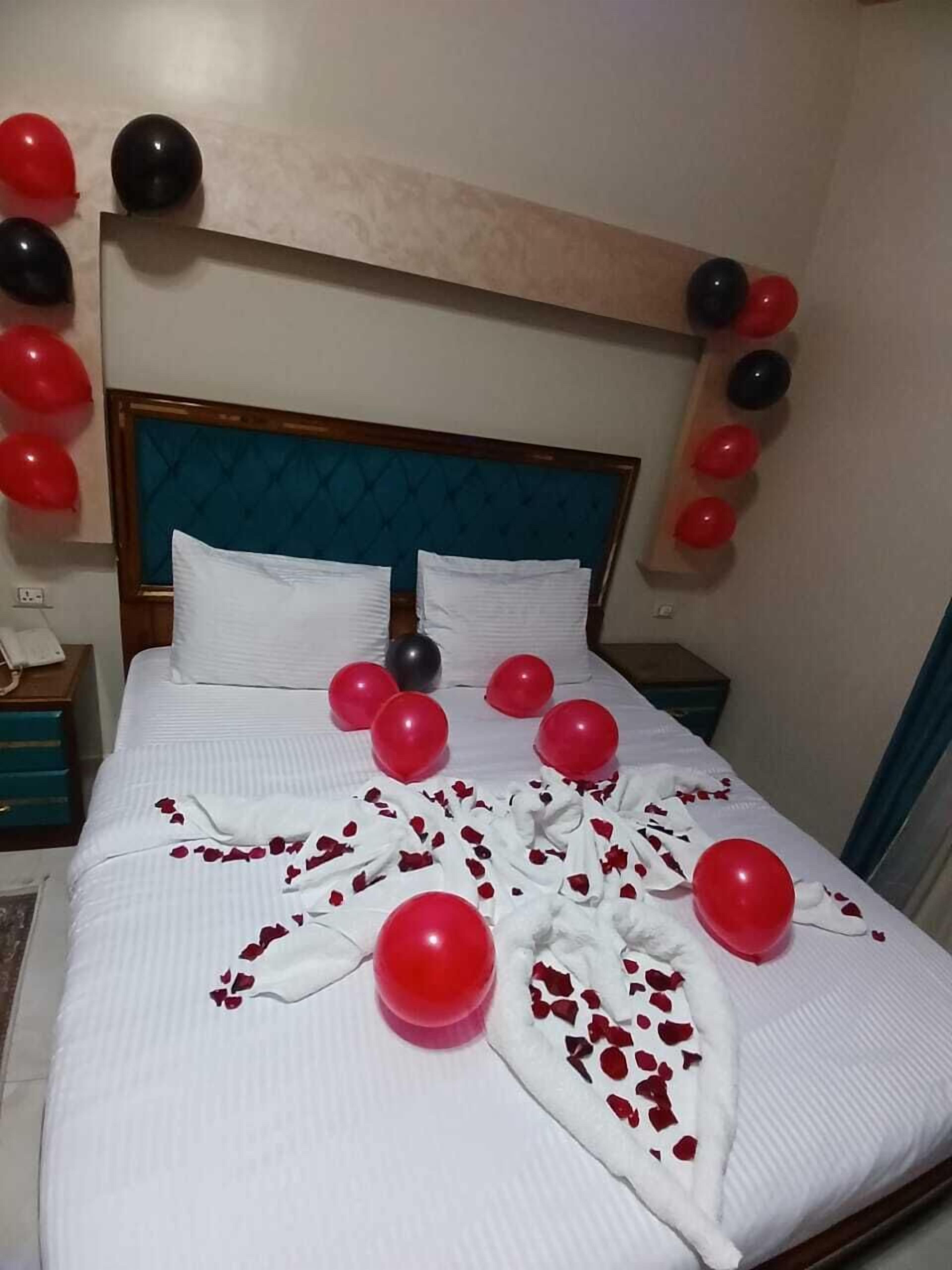 A bed with a white bedspread, red and black balloons, and a white towel with red rose petals.