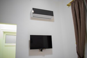 Une pièce avec un mur blanc, un climatiseur fixé au mur et un téléviseur à écran plat.