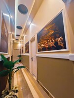 A hallway with framed artwork on the walls, a potted plant, and a window with a view of a building at night.