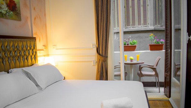 A hotel room with a bed, a small table with chairs, a balcony with potted plants, and a view of the street. - Golden Palace Hotel (Cairo)
