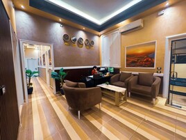 Un hall de hotel con mostrador de recepción, zona de estar y un cuadro grande en la pared.