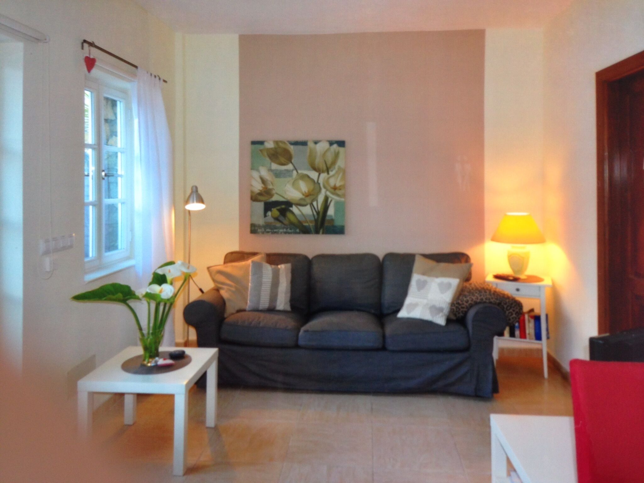 Un salon avec un canapé gris, une petite table blanche, un lampadaire et un tableau accroché au mur.
