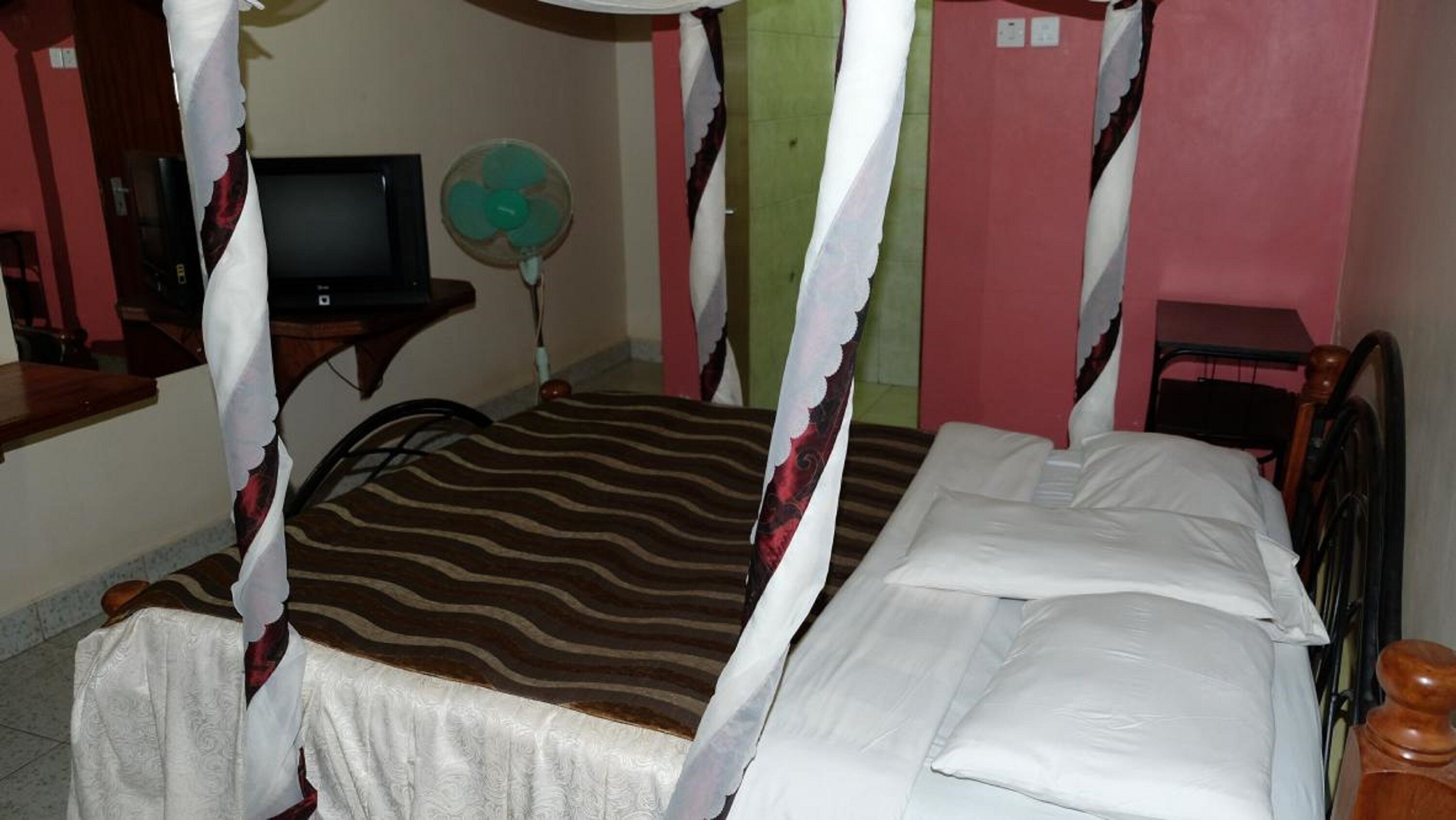 A room with a bed, a television, a fan, and a desk.