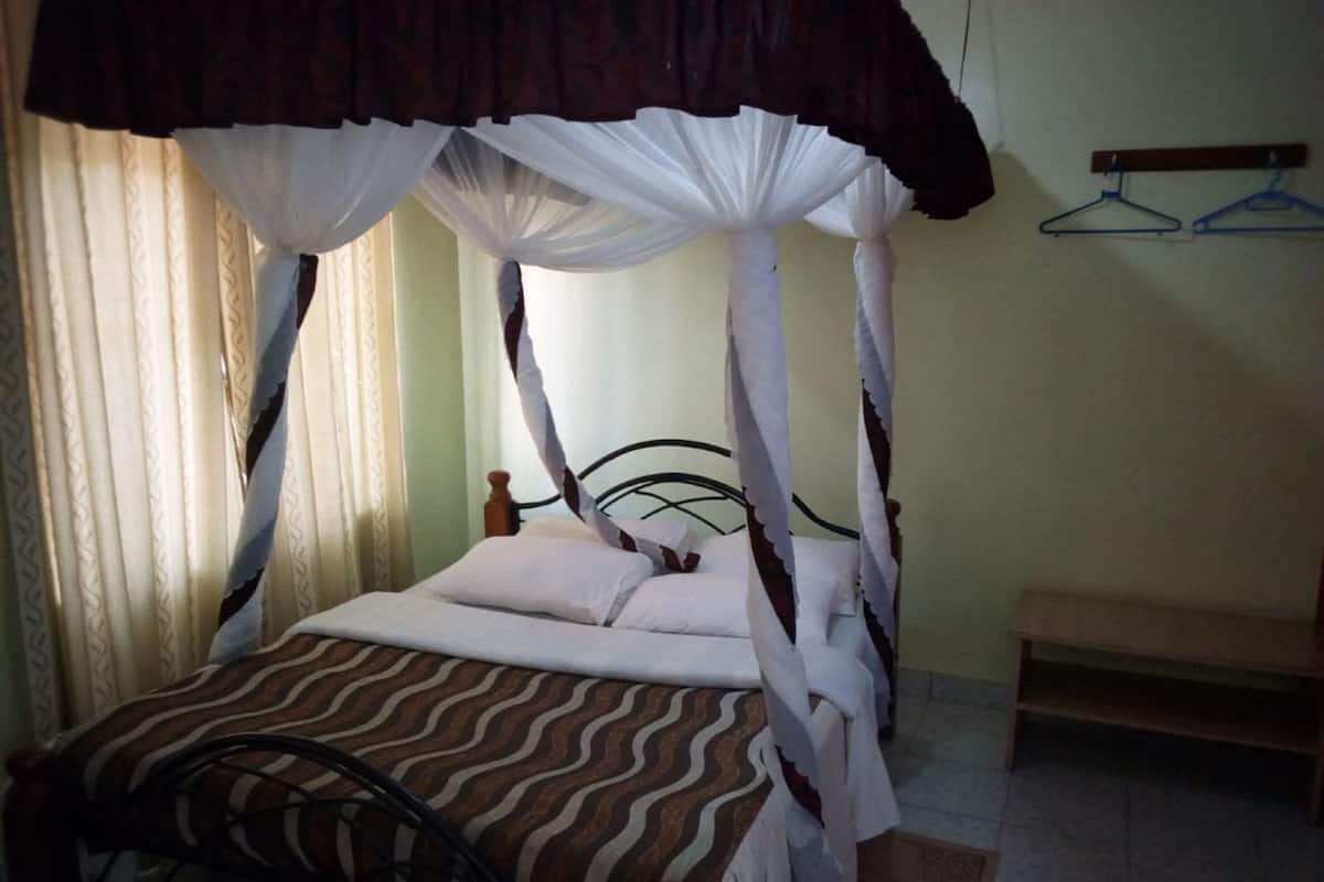 A single bed with a canopy, a bedside table, and a hanging clothes rack.
