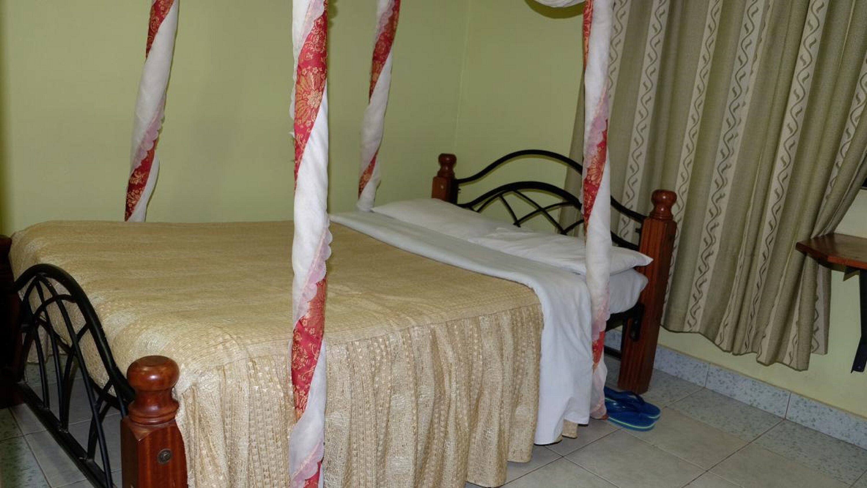 Un lit à baldaquin avec un couvre-lit blanc et des rideaux rouges et blancs, une tête de lit en bois et une petite table de chevet avec une lampe.