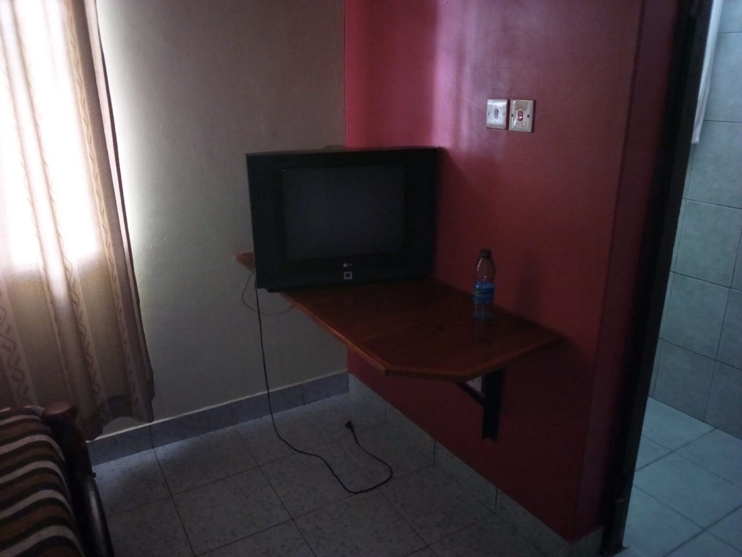 Une pièce avec un téléviseur posé sur un meuble en bois, une bouteille d’eau sur le meuble et une prise électrique au mur.
