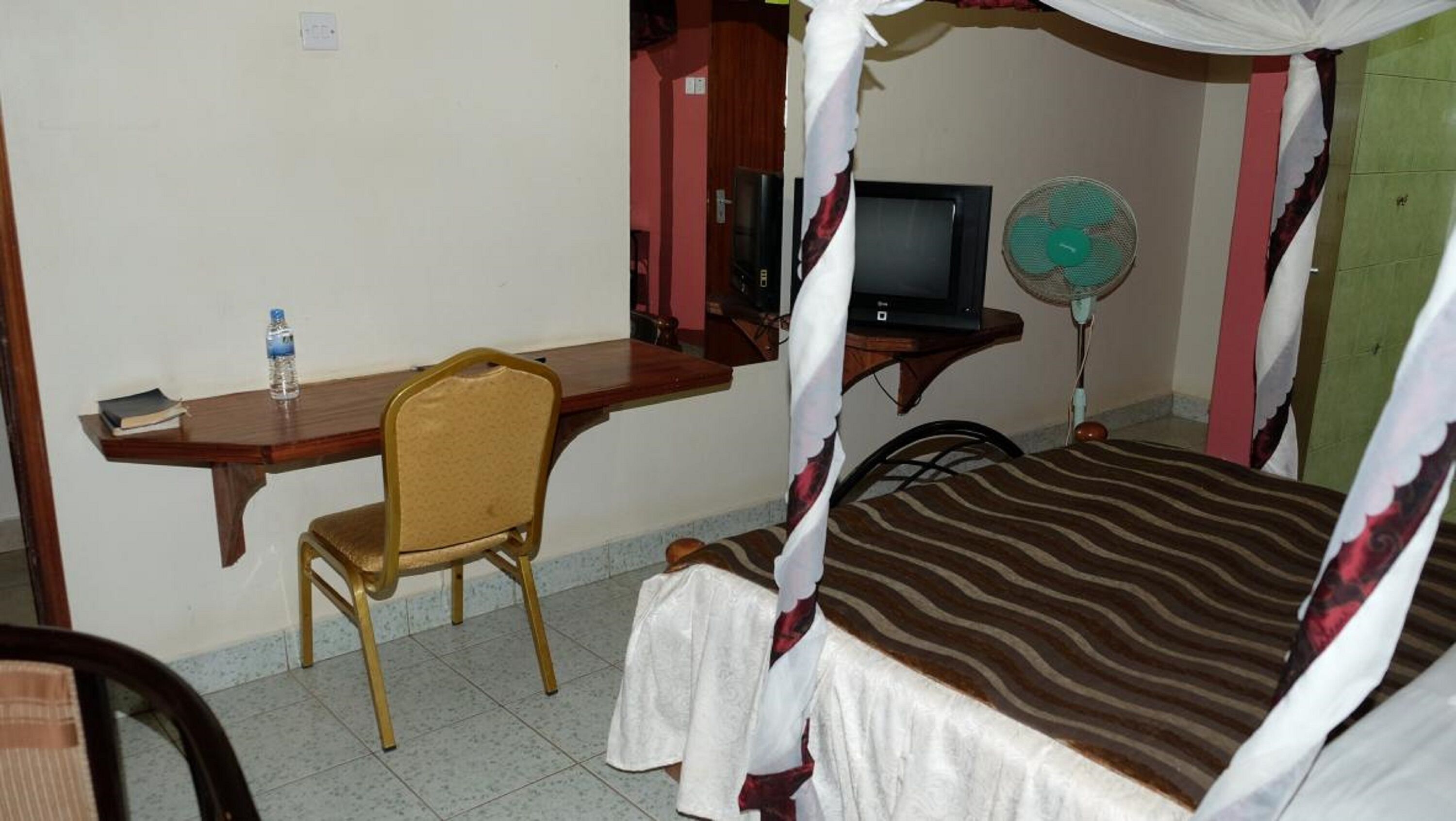 Een kamer met een bed, een bureau, een stoel, een televisie en een ventilator.