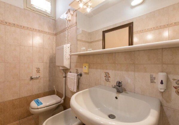 A bathroom with a toilet, bidet, sink, and a mirror above the sink. - Hotel Atlas (Rimini)