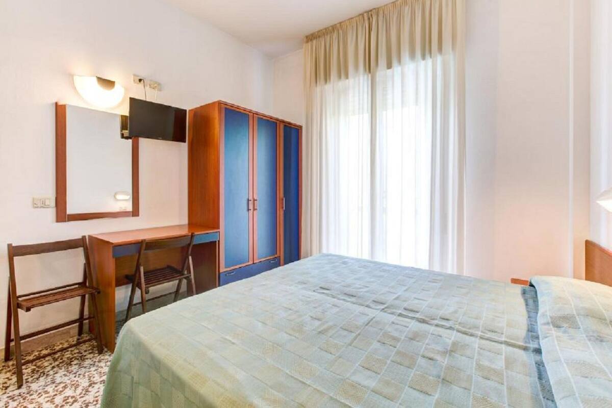 A hotel room with a bed, a desk, a chair, a wardrobe, and a mirror.