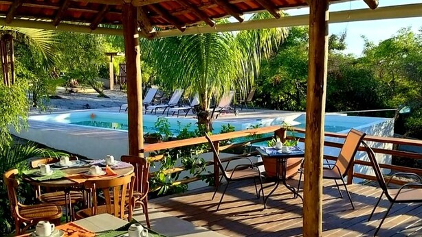 An outdoor dining area with tables set for a meal, overlooking a swimming pool and lush greenery.