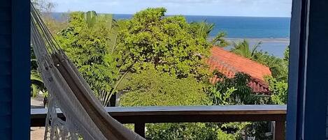 A hammock view from a balcony overlooking a lush green landscape and the ocean.