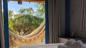 A bedroom with a bed, a hammock, and a view of palm trees.
