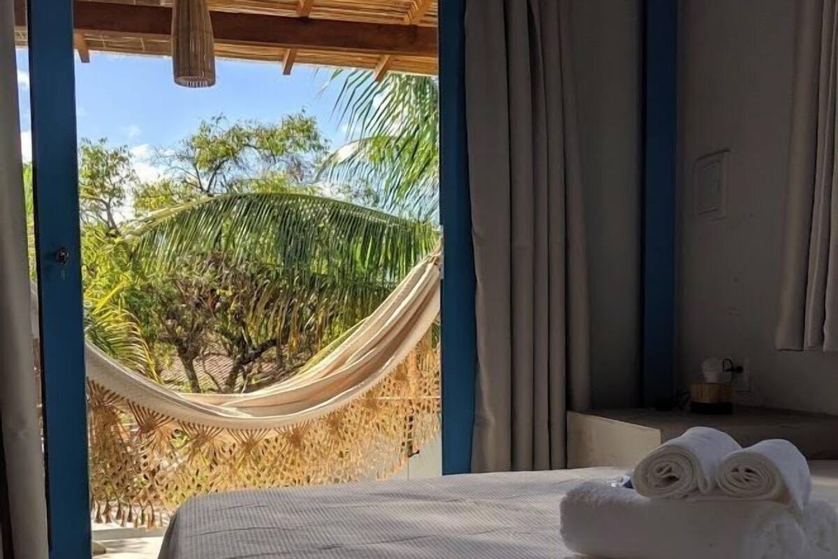 Ein Schlafzimmer mit einem Bett, einer Hängematte und Blick auf Palmen.