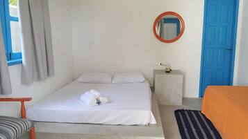 A bedroom with a bed, a round mirror, a blue door, and a window with curtains.