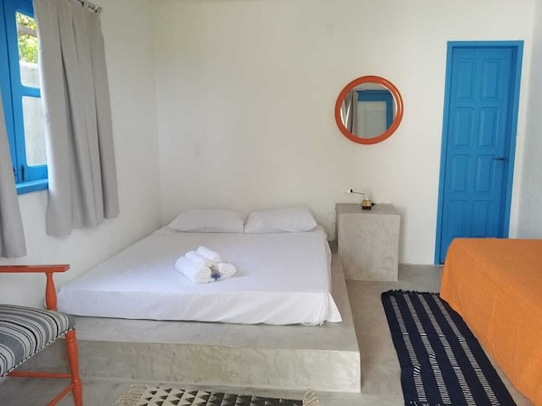A bedroom with a bed, a round mirror, a blue door, and a window with curtains.