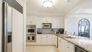 Una cocina moderna con armarios blancos, electrodomésticos de acero inoxidable, una encimera de granito y vistas al exterior a través de un amplio ventanal de arco.