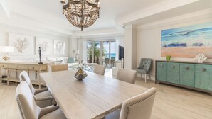 Un comedor amplio con una mesa y sillas de madera, un candelabro y vista al océano a través de amplios ventanales.